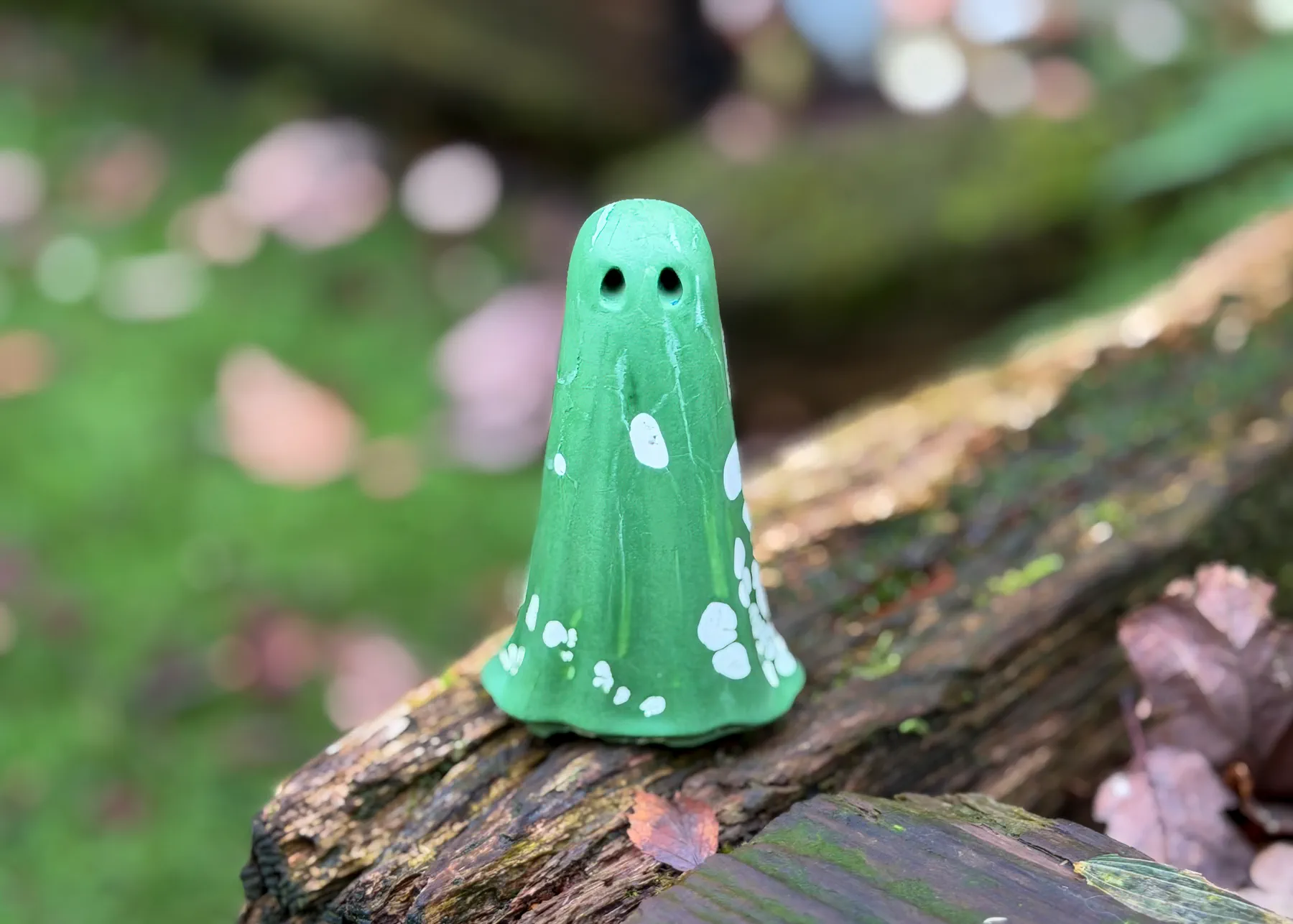 Fortuna Light Haunt green handmade ghost figurine with white markings resting on a fallen tree in a woodland setting