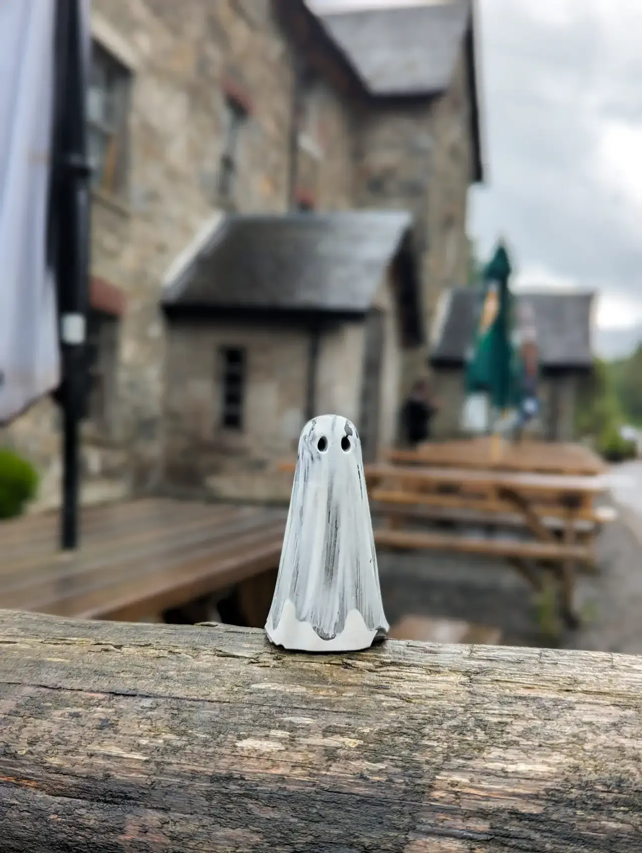 White and grey Requiem Haunt ghost figurine standing on a weathered wooden railing outside a traditional stone building.