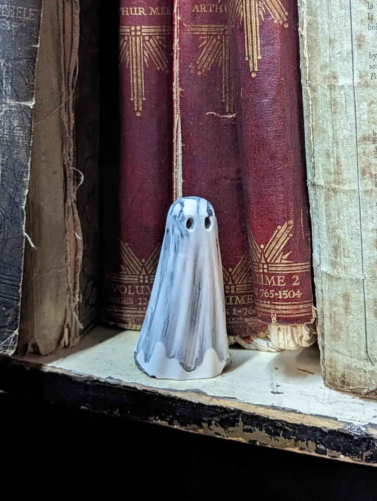 Requiem handmade Shadow Haunt ghost figurine with grey markings displayed among vintage books on a rustic shelf.